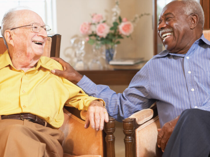 Assisted-Lifestyle Two senior men sitting in chairs and smiling while talking to each other