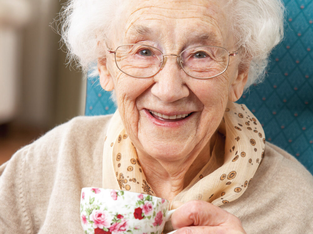 Happy-Senior-Woman-Enjoying-a-Cup-of-Tea Happy senior woman drinking a warm cup of tea inside