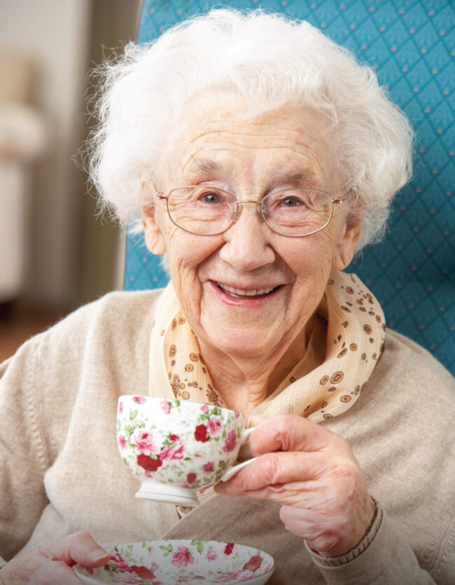 Happy-Senior-Woman-Enjoying-a-Cup-of-Tea Happy senior woman drinking a warm cup of tea inside