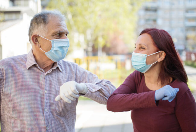elbow-Bump Senior man and female staff worker both wearing gloves and masks elbow bump.
