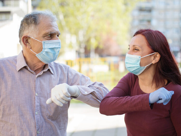 elbow-Bump Senior man and female staff worker both wearing gloves and masks elbow bump.